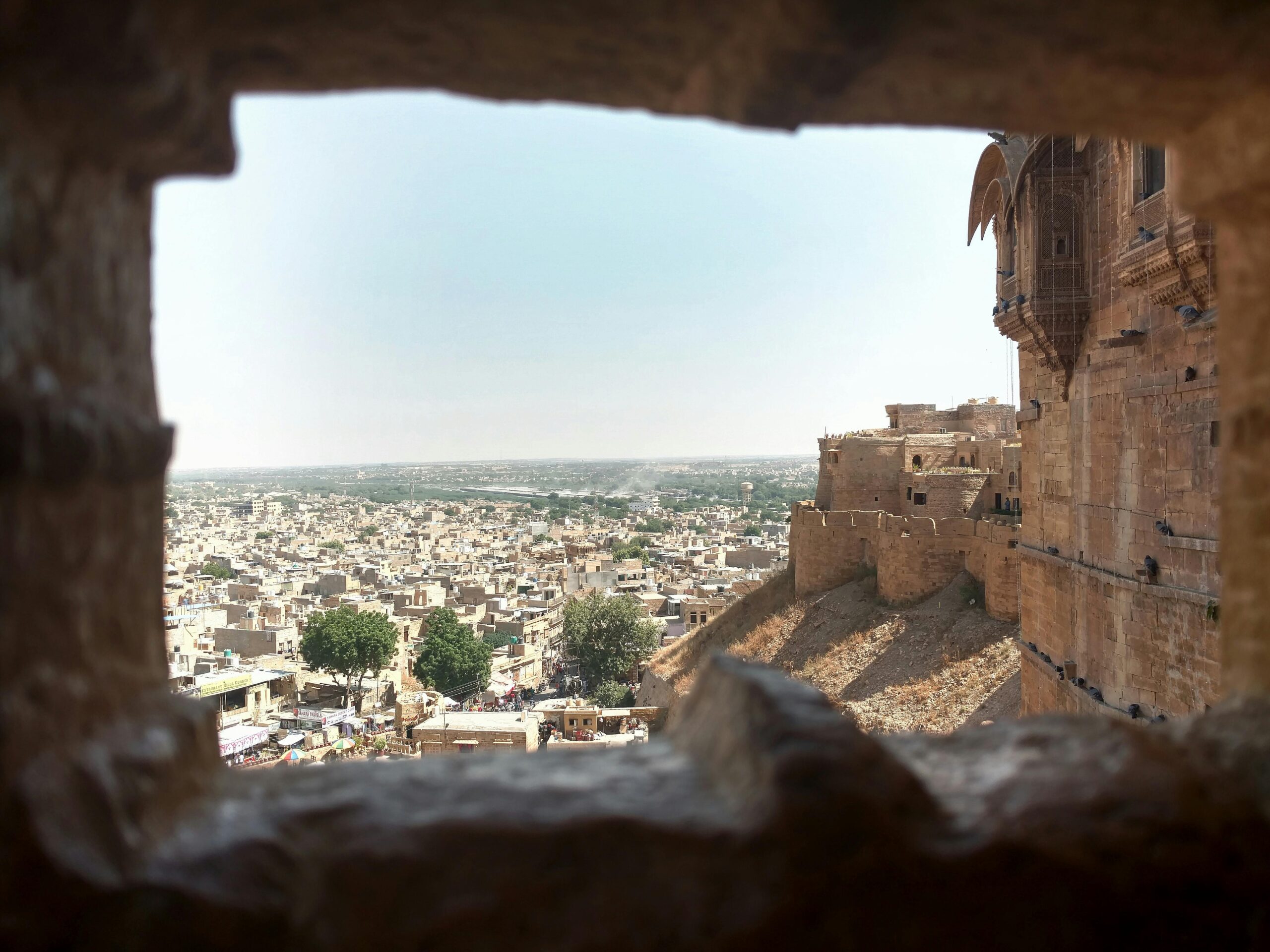 Distant ancient stone buildings of aged town with wall of medieval fort in India